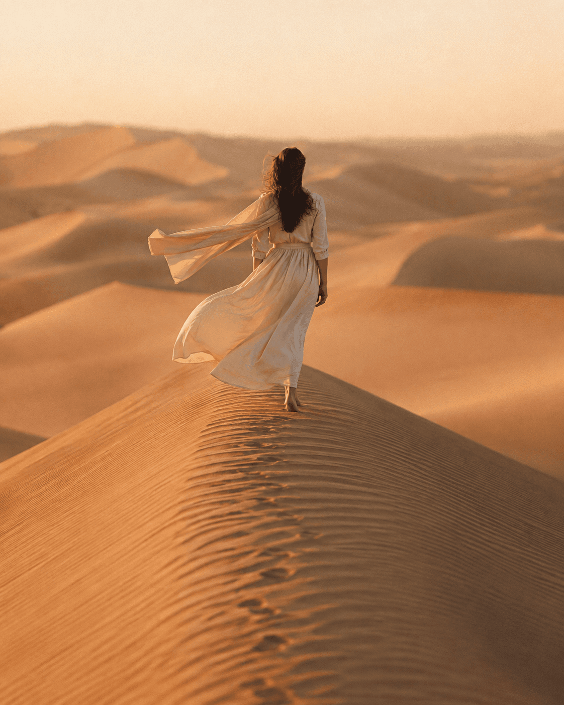 A traveller in flowing linen walking the crest of a sand dune at golden hour